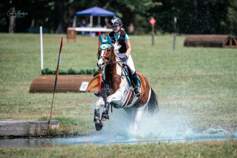 A paint horse and rider in teal splashing through the water complex on the cross-country course